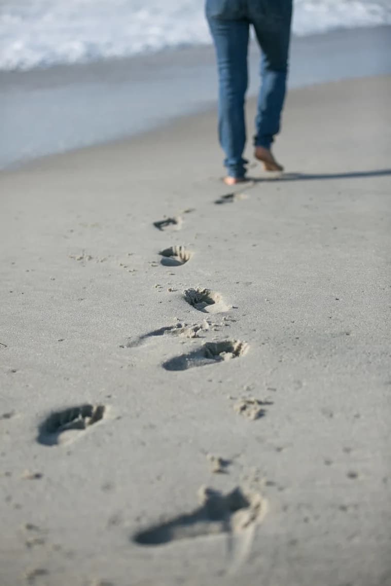 Footprints in the sand leading toward someone walking along the beach