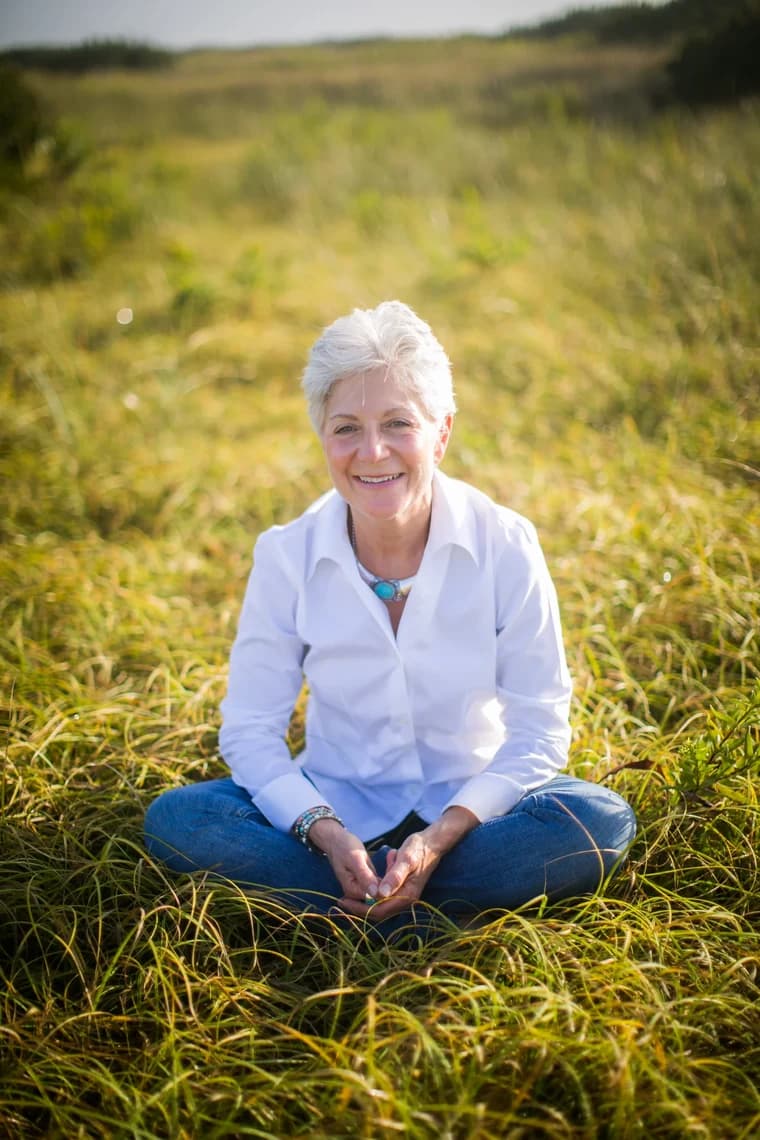 Nancy Devine sitting cross-legged in tall grass, smiling